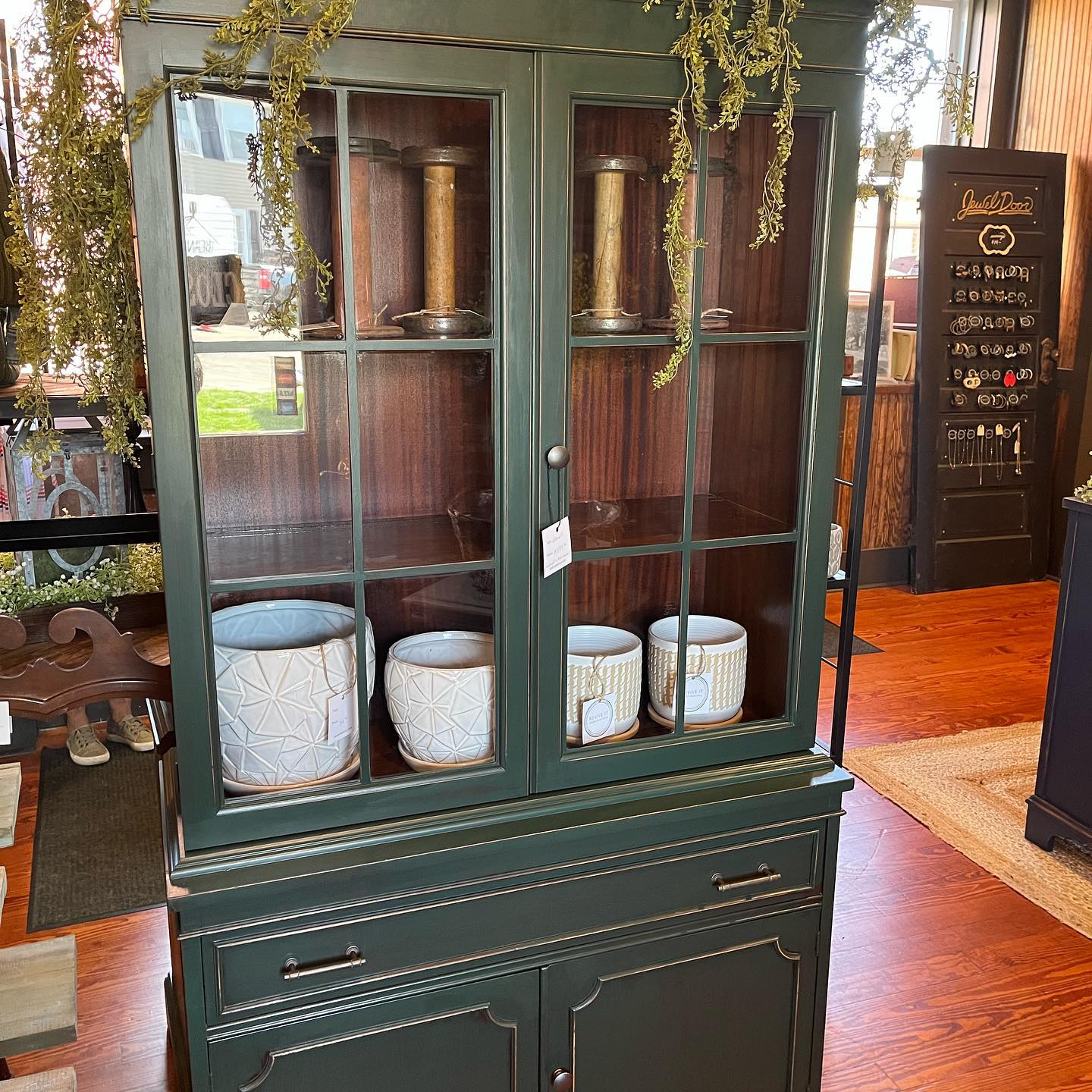 Green cabinet with glass doors displaying decorative items on a wooden floor.