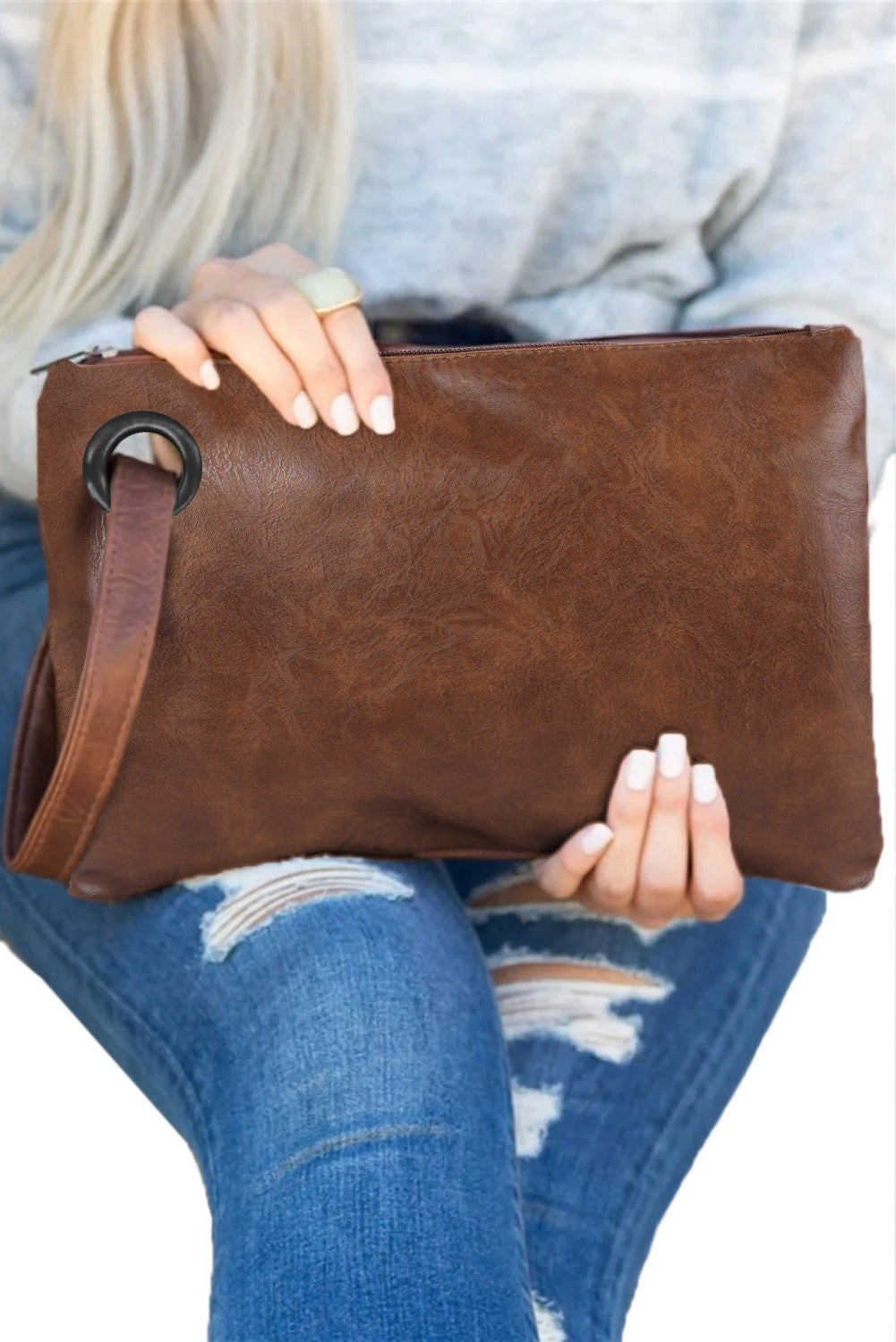 Brown leather clutch held by a person wearing blue jeans on a white background