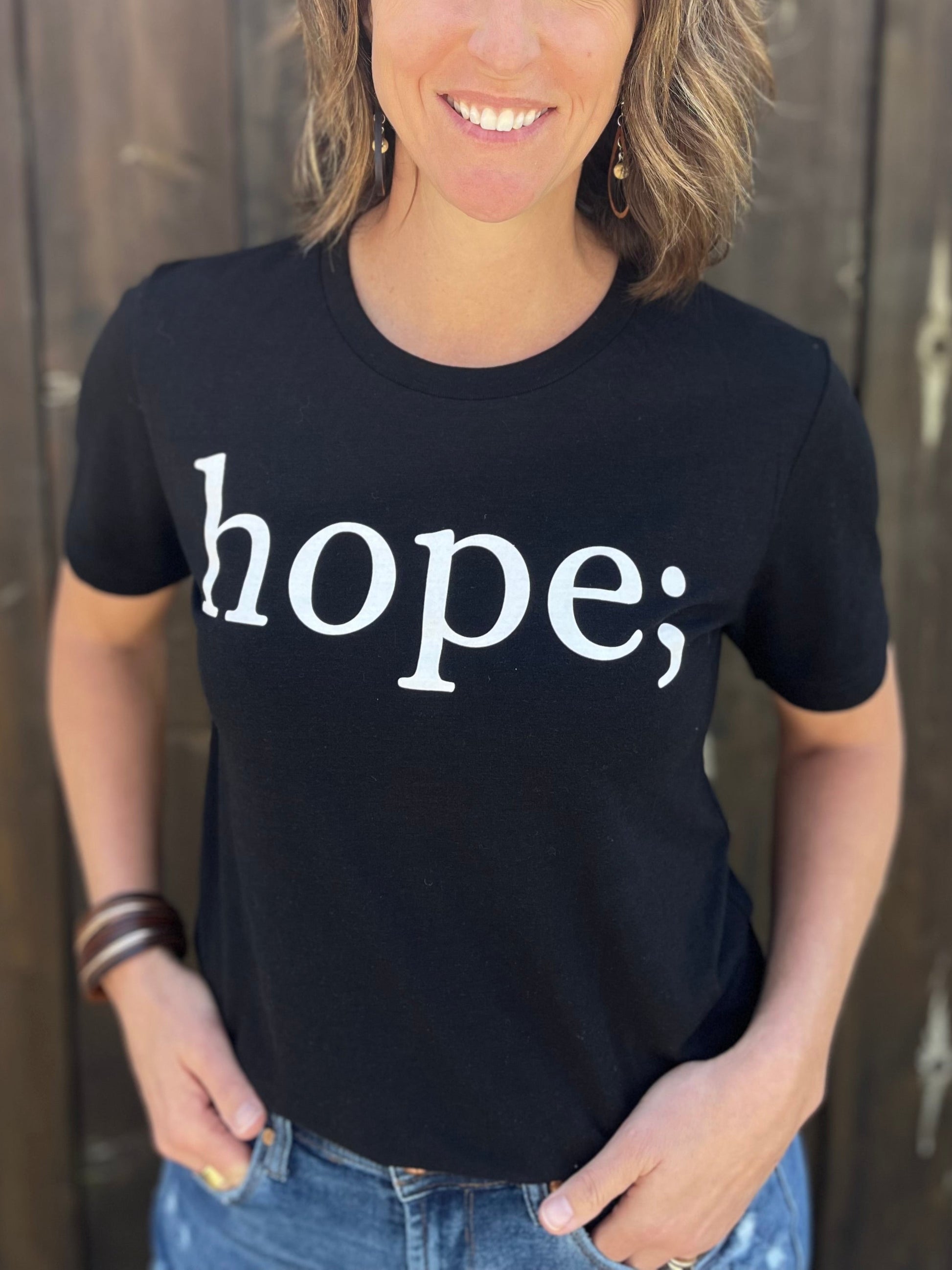A person wearing a black T-shirt with the text 'hope;' written in white.