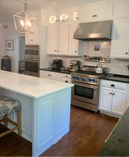 Modern kitchen with white cabinets, stainless steel appliances, and a marble island.